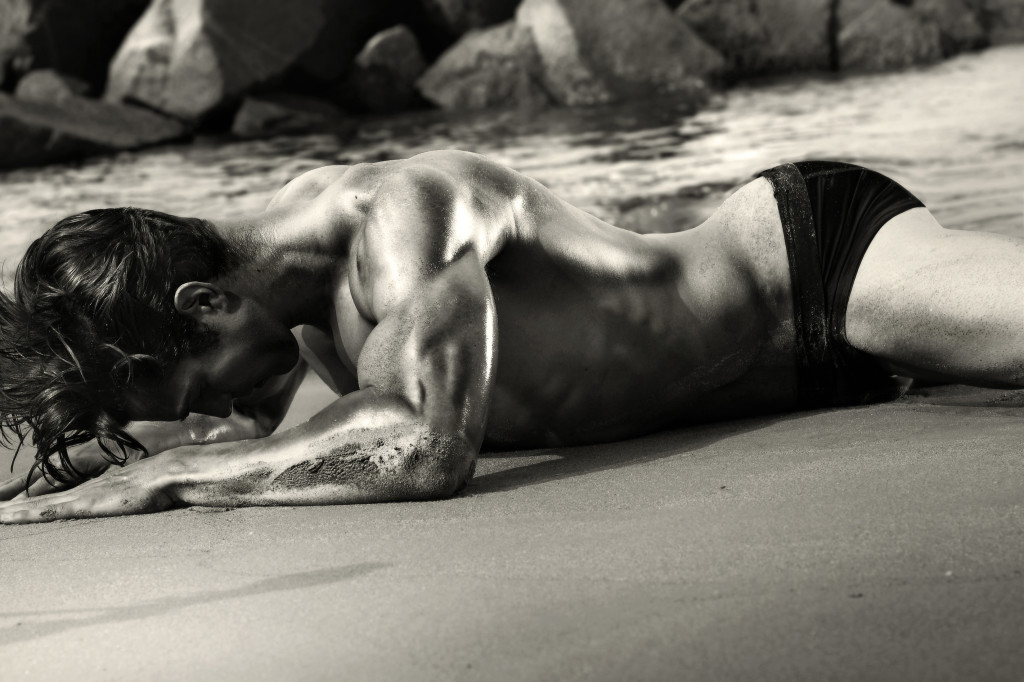 Sexy black and white image of man crawling on beach in only his black briefs.